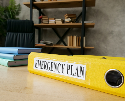 A yellow binder with the words, "Emergency Plan" on the side of it. The folder is sitting on a desk in an office.