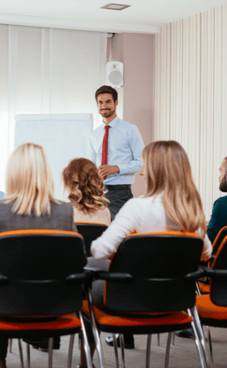 A smiling person in front of a room of employees conducting a training session.