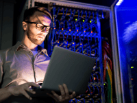 A tech working in a dark server room on a computer.