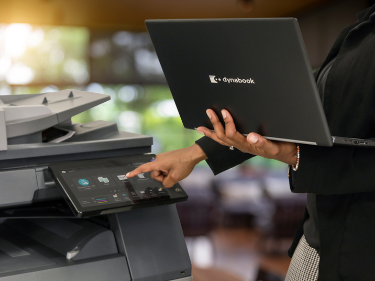 A person with a Dynabook laptop at a multifunctional printer.