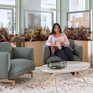 A person reading a book while sitting on a comfy chair that is next to an identical chair and a coffee table.