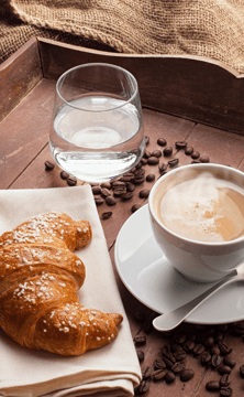 A croissant next to a cup of coffee. Behind the two is a glass of water.