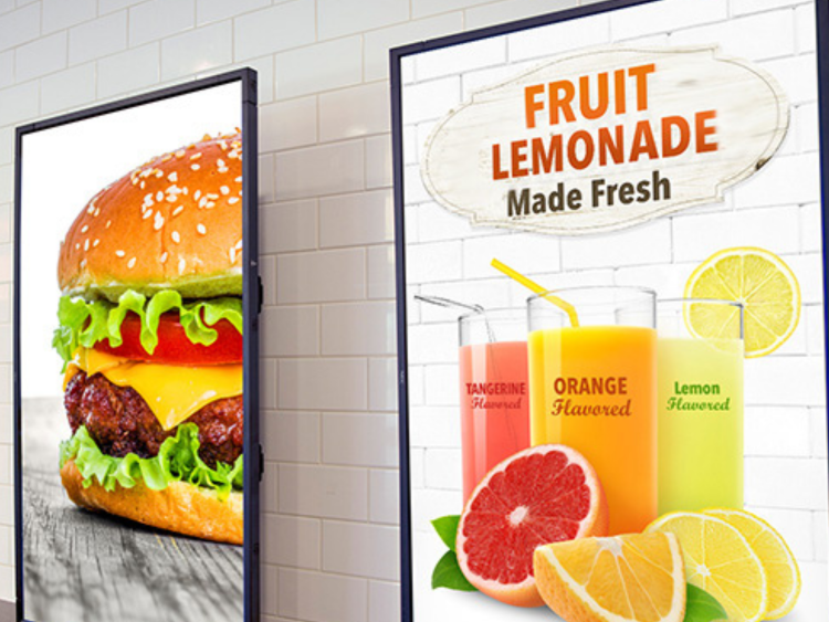 A photo of two vertical video displays. On the left is a display showing a cheese burger. On the right display it shows fresh fruit lemonade in glasses with fruit in front of them. 