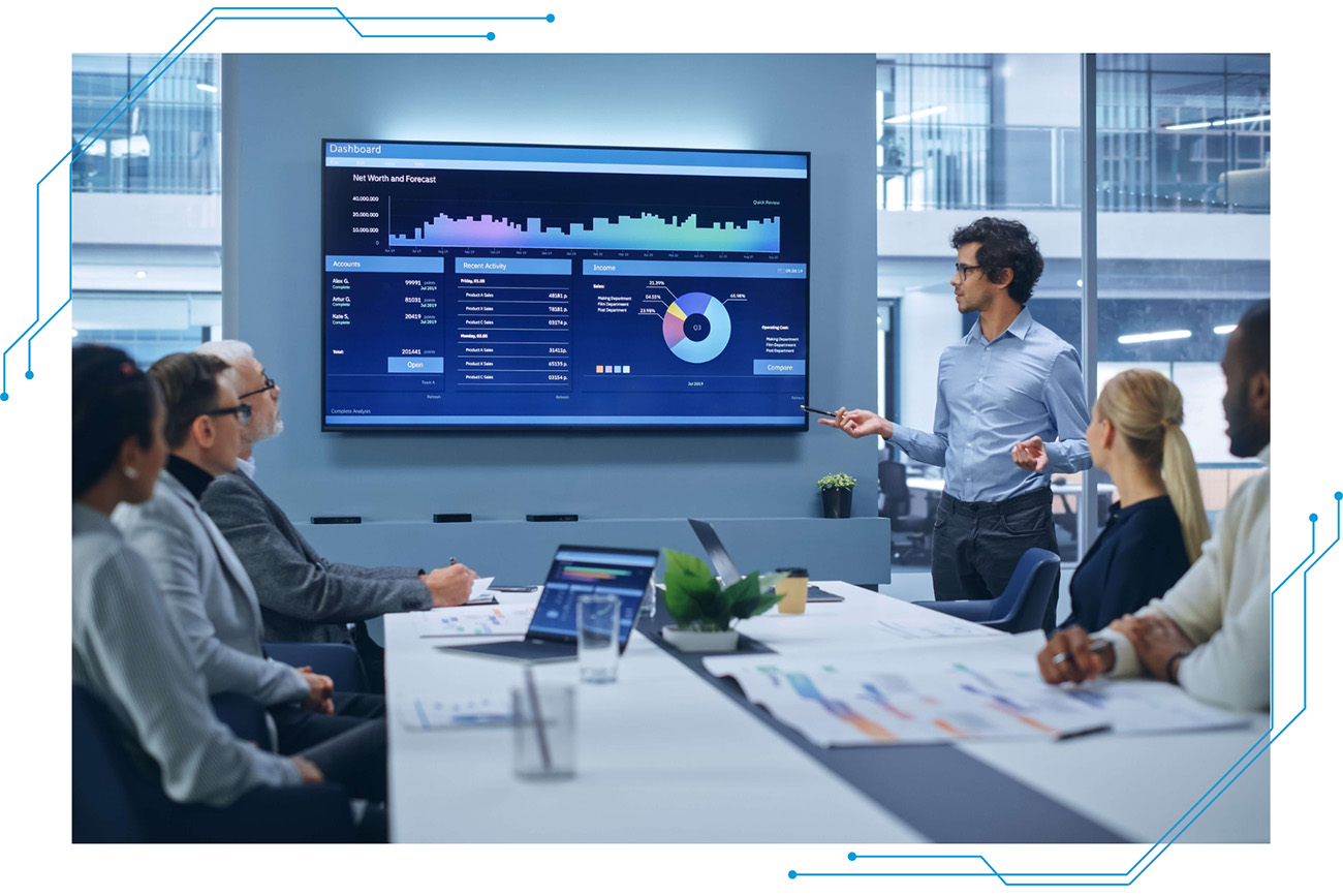 Employees sitting at a conference table looking at charts on a screen.