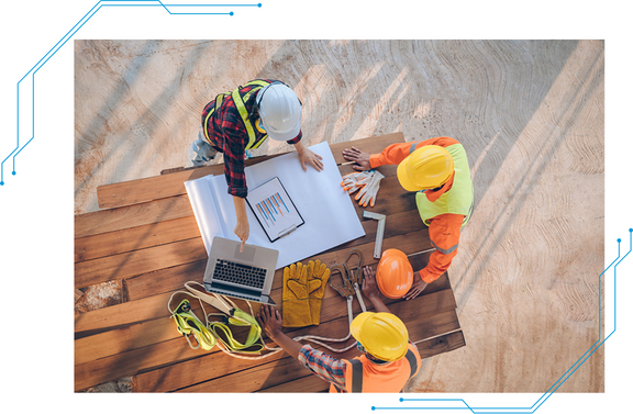 Three construction workers looking at a laptop and plans at a job site.