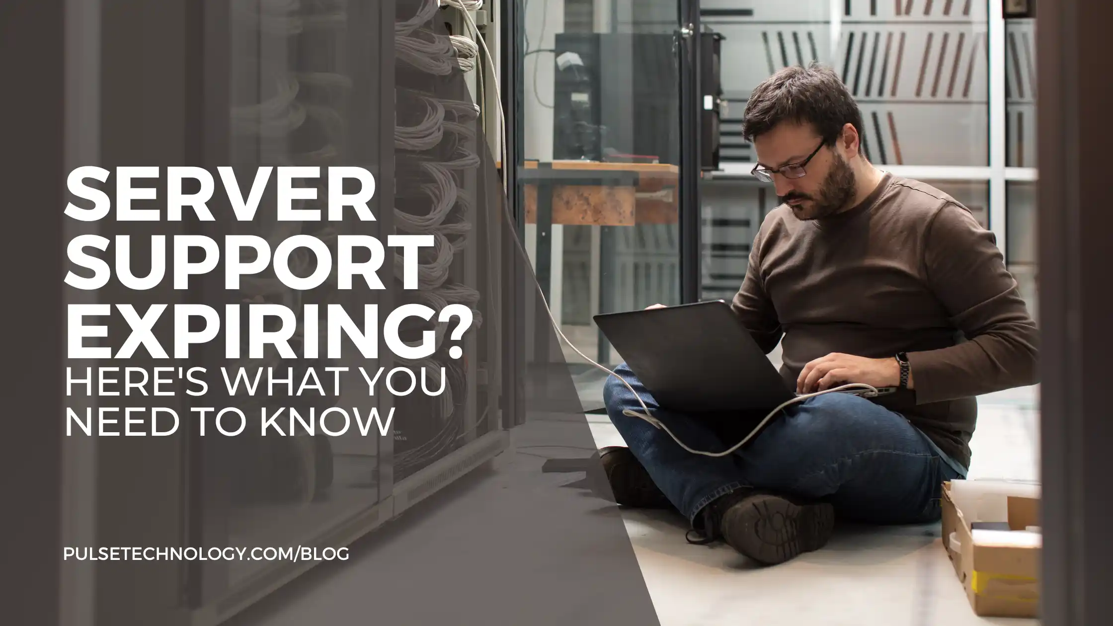 A tech expert sitting on the floor in a server room working on a laptop.